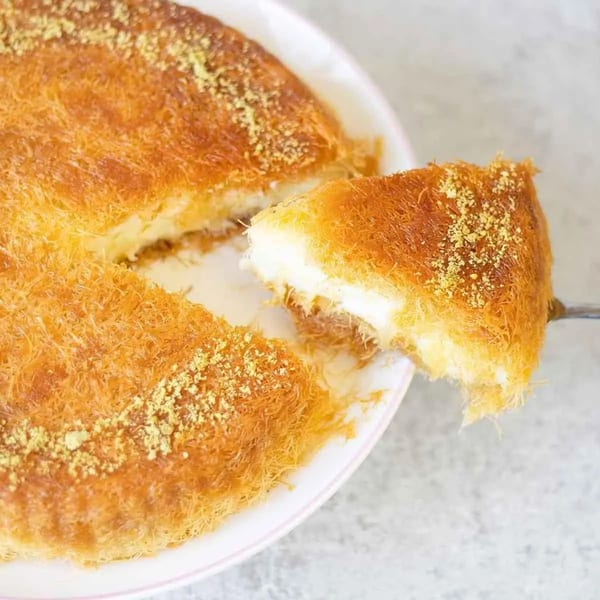 A golden-brown kunafa with a slice being lifted, revealing its creamy white cheese filling.