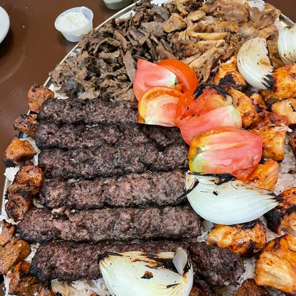 A large platter of Erbil Kabob's grilled meats, including kabobs, chicken, and shawarma, with rice, tomatoes, and onions.