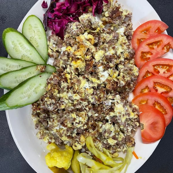 Erbil Kabob's scrambled eggs with ground meat, sliced cucumbers, tomatoes, and pickled vegetables.