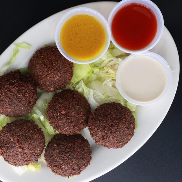 Six falafel patties on lettuce with three dipping sauces on a white plate.