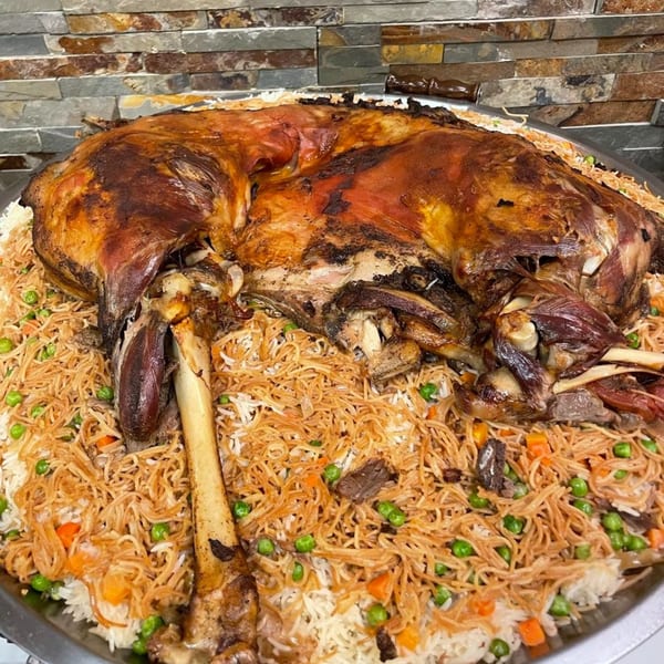A whole roasted lamb, golden brown and crispy, served on a bed of rice with peas and carrots.