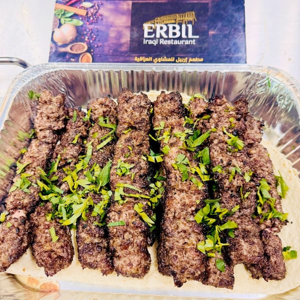 Erbil Kabob's grilled kabobs, garnished with fresh herbs, served in a foil tray over flatbread.