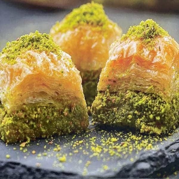 Three pieces of Erbil Kabob's baklava, topped with green pistachio crumbles, on a dark plate.